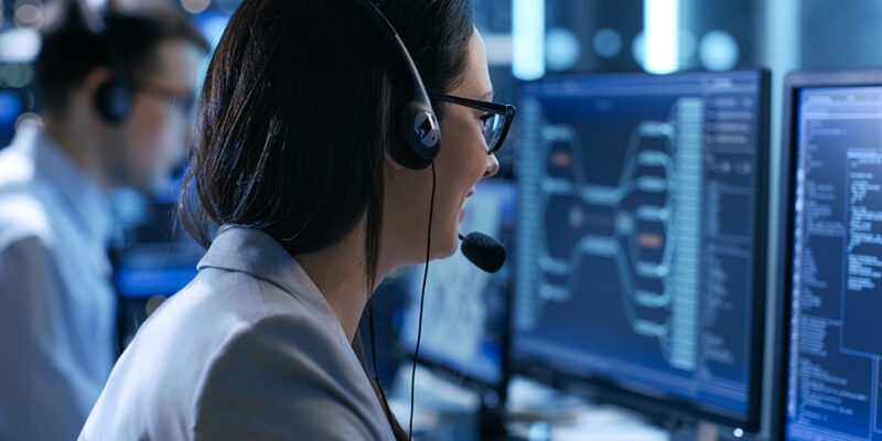 In the System Control Center Woman working in a Technical Support Team Gives Instructions with the Help of the Headsets. Possible Air Traffic/ Power Plant/ Security Room Theme.
